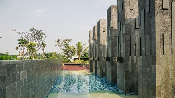 A swimming pool with a tiled floor and a stone wall on one side. - Minimalist And Comfy 1Br Citralake Suites Apartment (Jakarta)