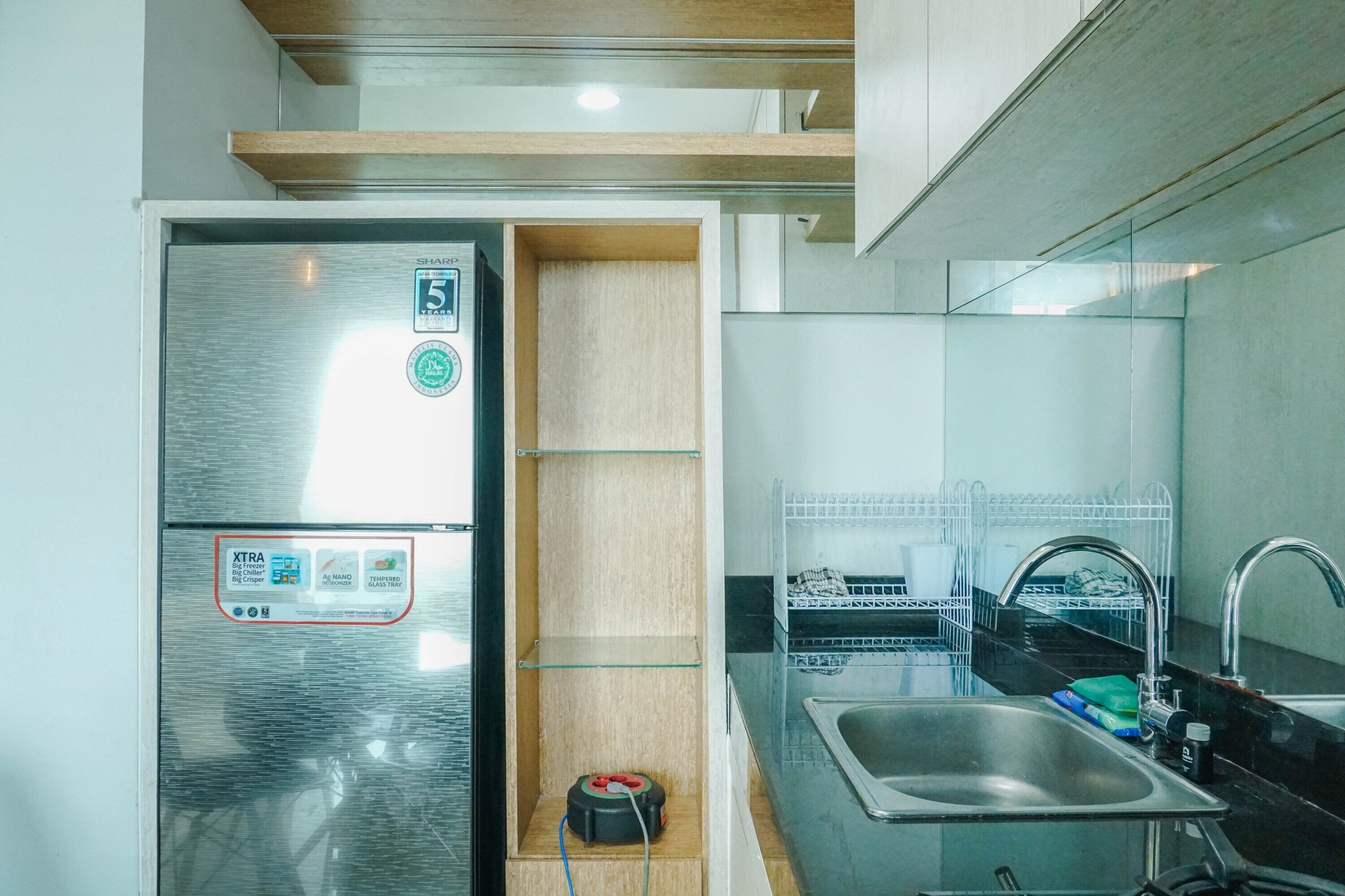 A compact kitchen with a stainless steel refrigerator, a sink, and a dish drying rack.