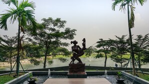 A statue of a woman holding a child on a platform with a pond in the foreground.