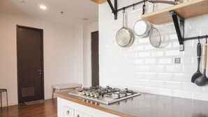 A kitchen with a gas stove, white cabinets, and a wooden countertop. There is a door and a bench in the background. - Nice And Homey 1Br At Citralake Suites Apartment (Jakarta)