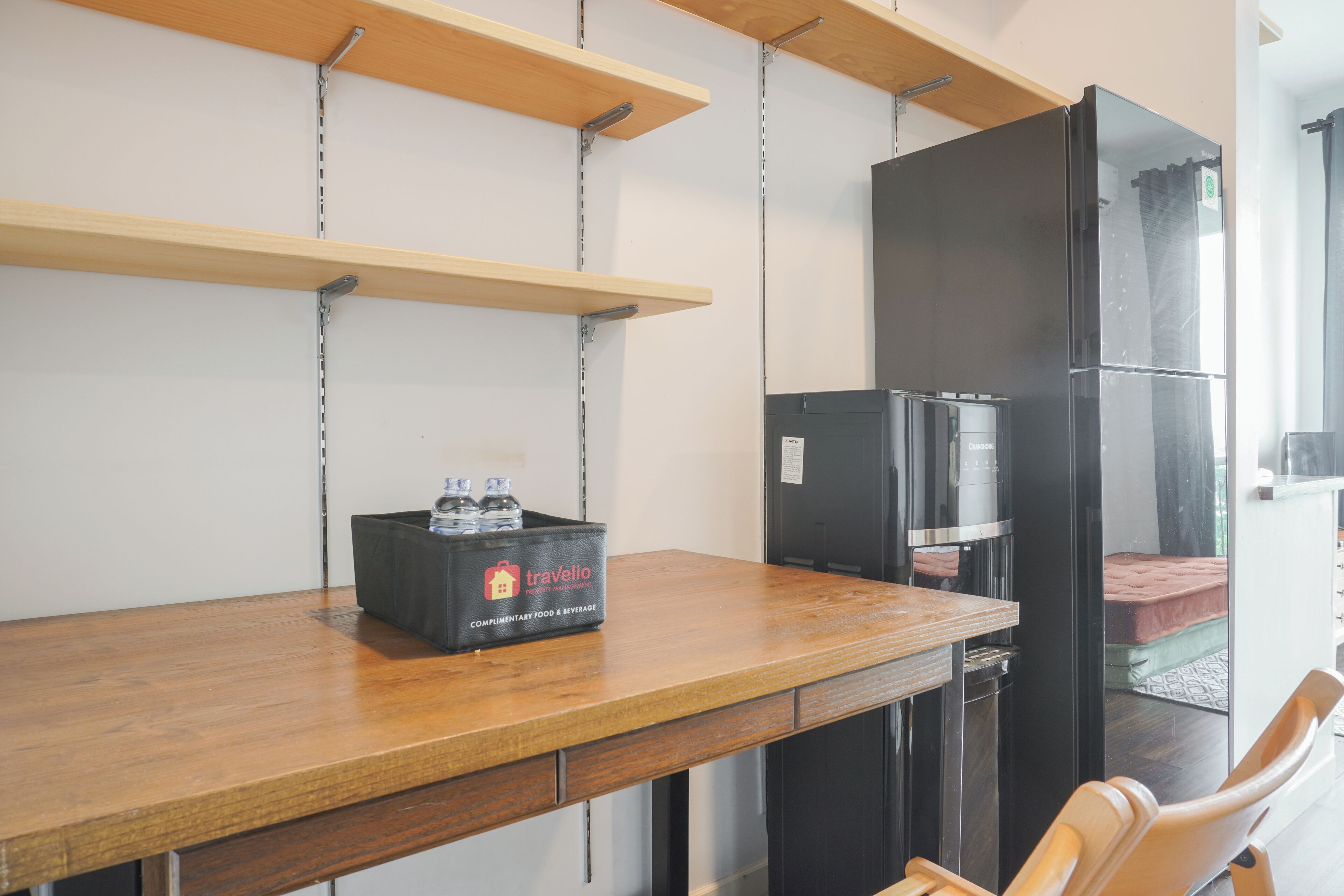 Une petite cuisine équipée d’un plan de travail en bois, d’un réfrigérateur noir et d’une boîte de boissons de la marque Travelio.
