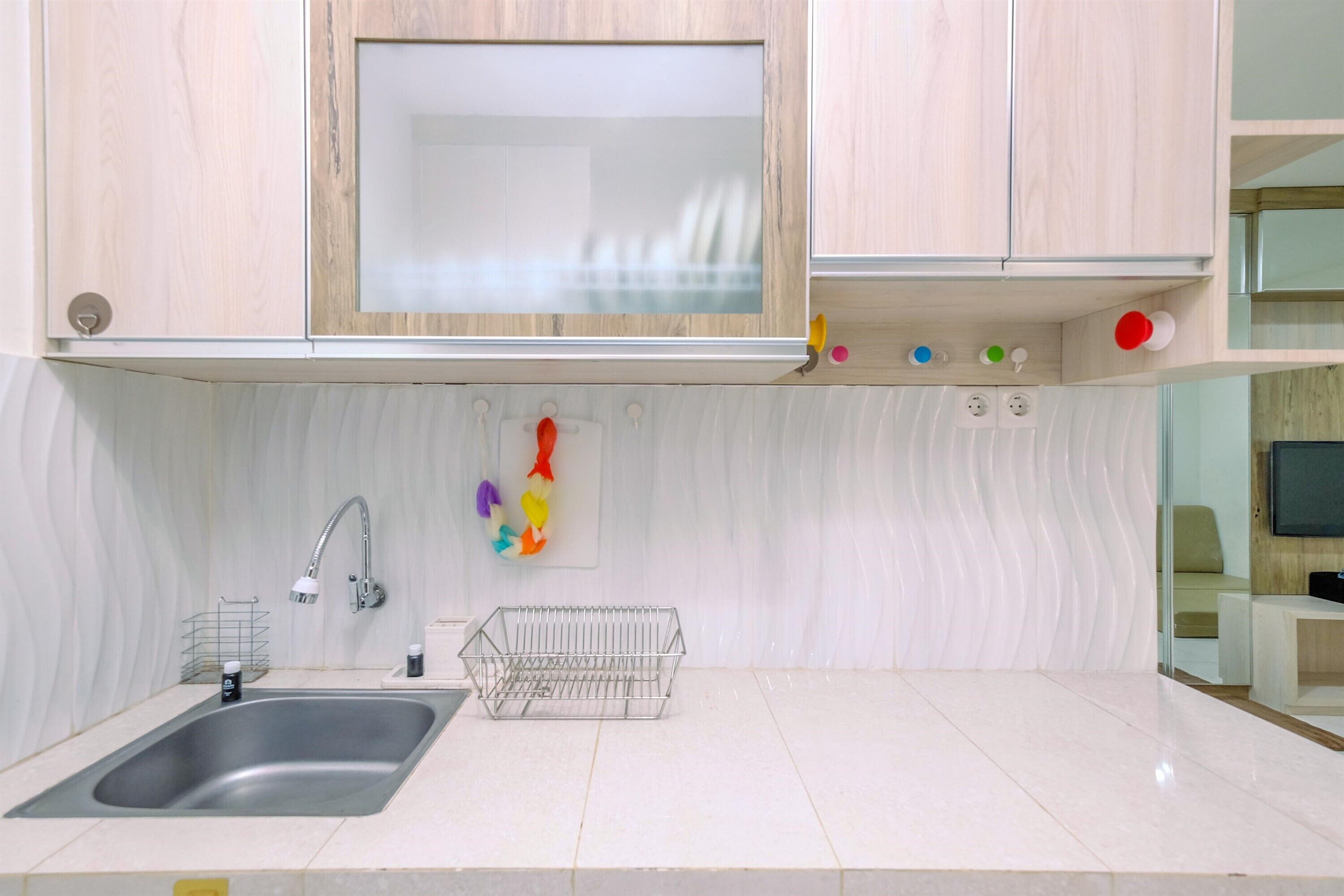 A modern kitchen with a stainless steel sink, wooden cabinets, a white tiled backsplash, and a small wire basket.
