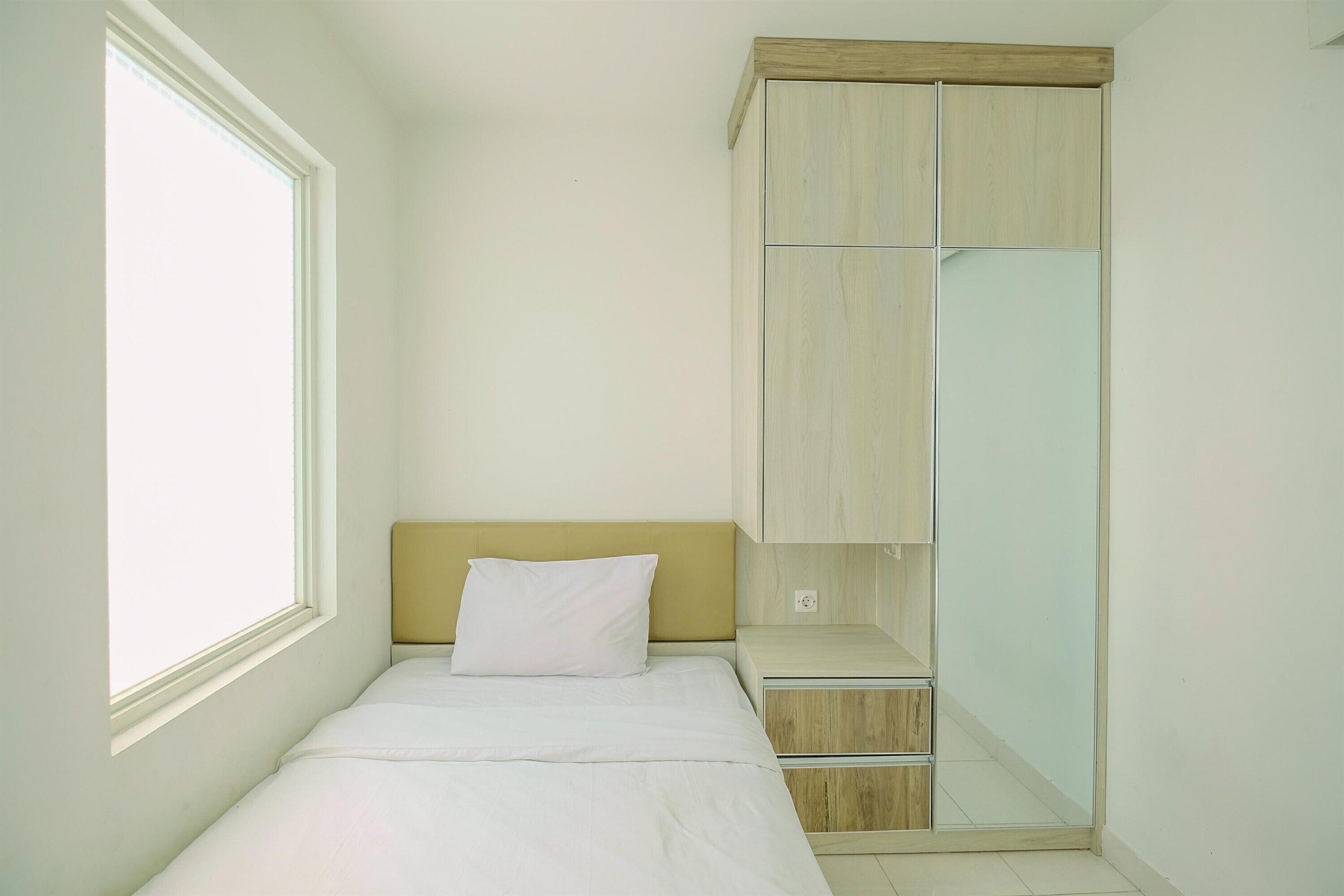 A small, single-bed room with a wooden headboard, a bedside table, and a wardrobe with mirrored doors.