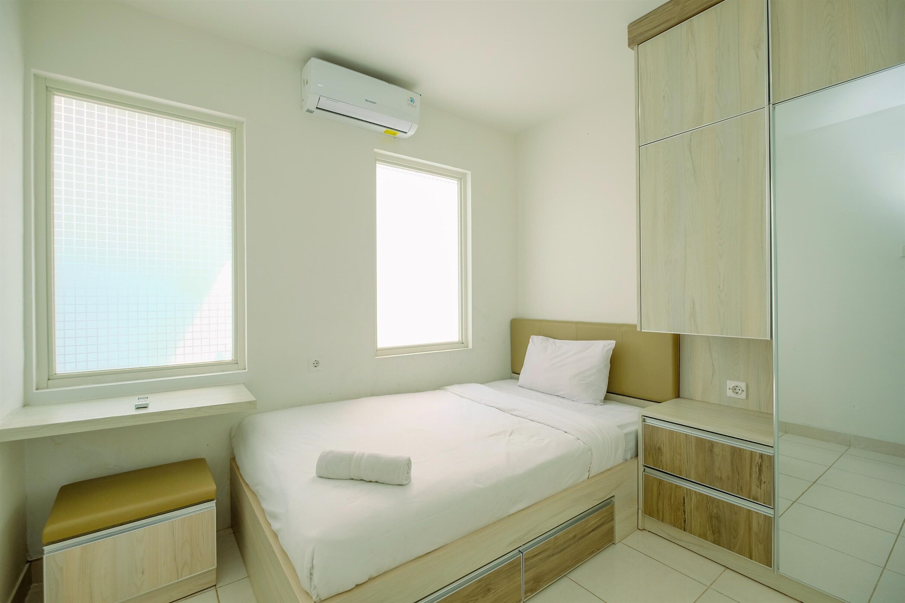 Un dormitorio pequeño y bien iluminado con una cama individual, una ventana, un banco empotrado y un armario.