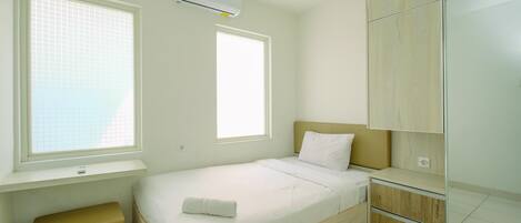 Un dormitorio pequeño y bien iluminado con una cama individual, una ventana, un banco empotrado y un armario.