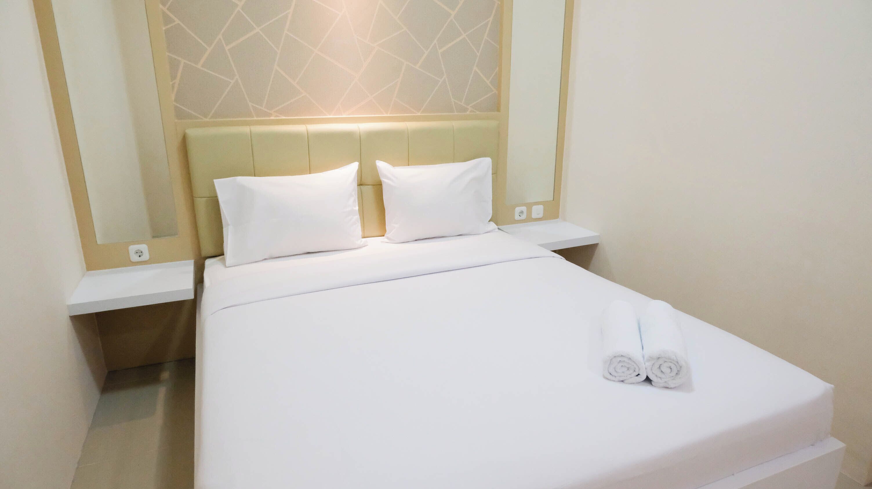 Un lit bien fait, avec du linge de lit blanc et des oreillers, une table de chevet et un miroir fixé au mur.