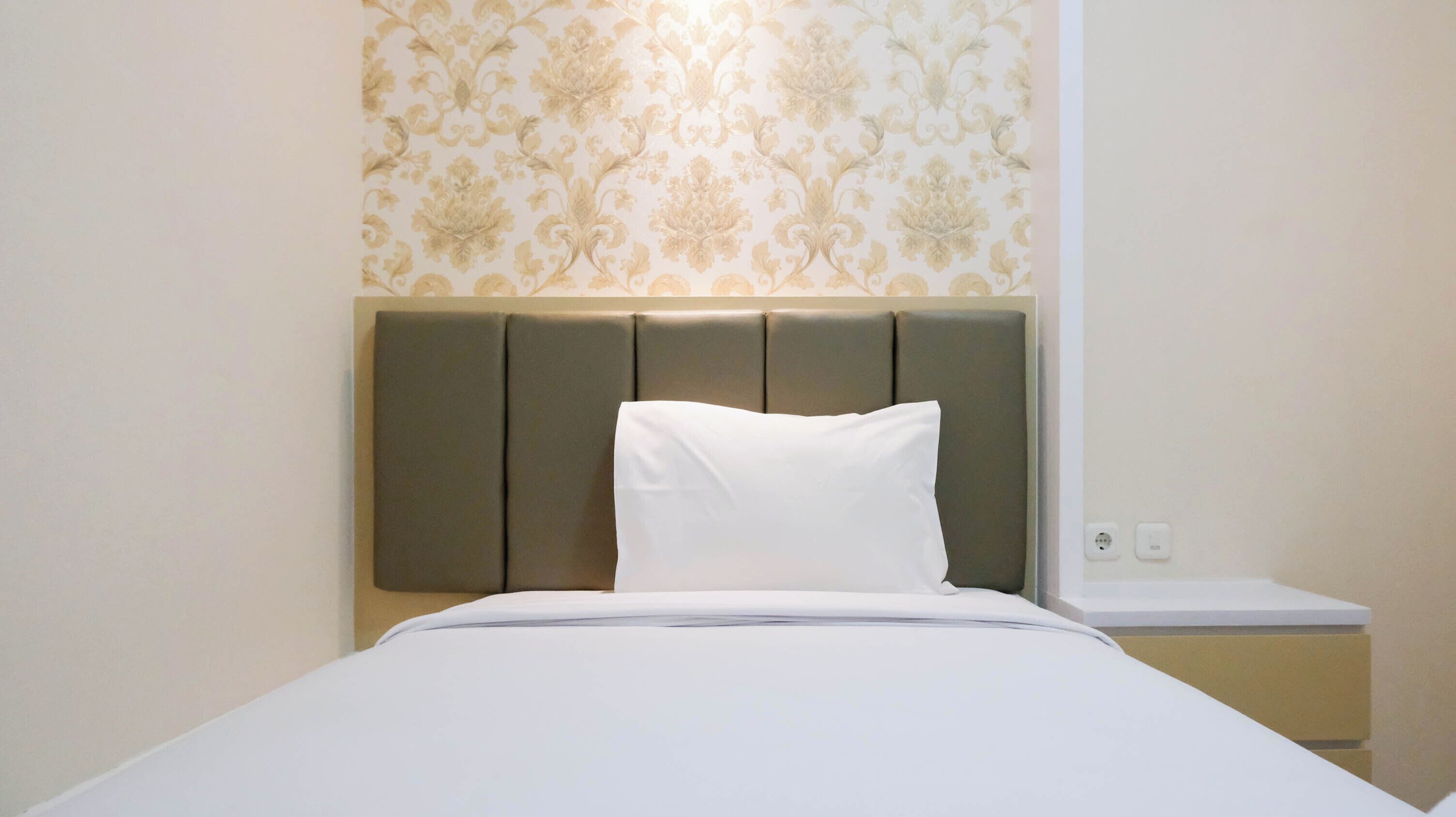A neatly made bed with a white pillow and a headboard with a light brown panel.