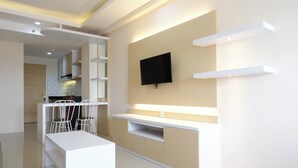 A modern kitchen with white cabinetry, a dining area with a white table and chairs, and a flat-screen TV mounted on the wall.