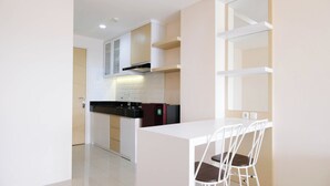 A modern kitchen with white cabinets, a black countertop, and a built-in stove. There is a refrigerator and a sink. A white dining table with two chairs is visible.