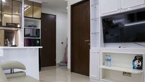 A modern living room with a flat-screen TV, a sofa, a coffee table, and built-in shelves with a microwave and a vacuum cleaner.