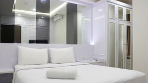 A neatly made bed with white linens and a rolled towel, a large mirror above the bed, and a wardrobe with glass doors.