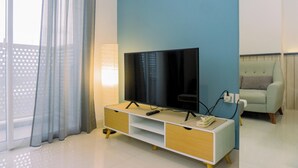 Una sala de estar moderna con una televisión de pantalla plana sobre un mueble blanco y de madera, una pared azul claro, un reloj y un sofá de color claro.