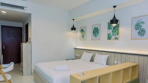 Una habitación de hotel moderna con una cama grande, una mesita de noche de madera, un escritorio y una silla. Hay cuadros en la pared y una lámpara en el techo.