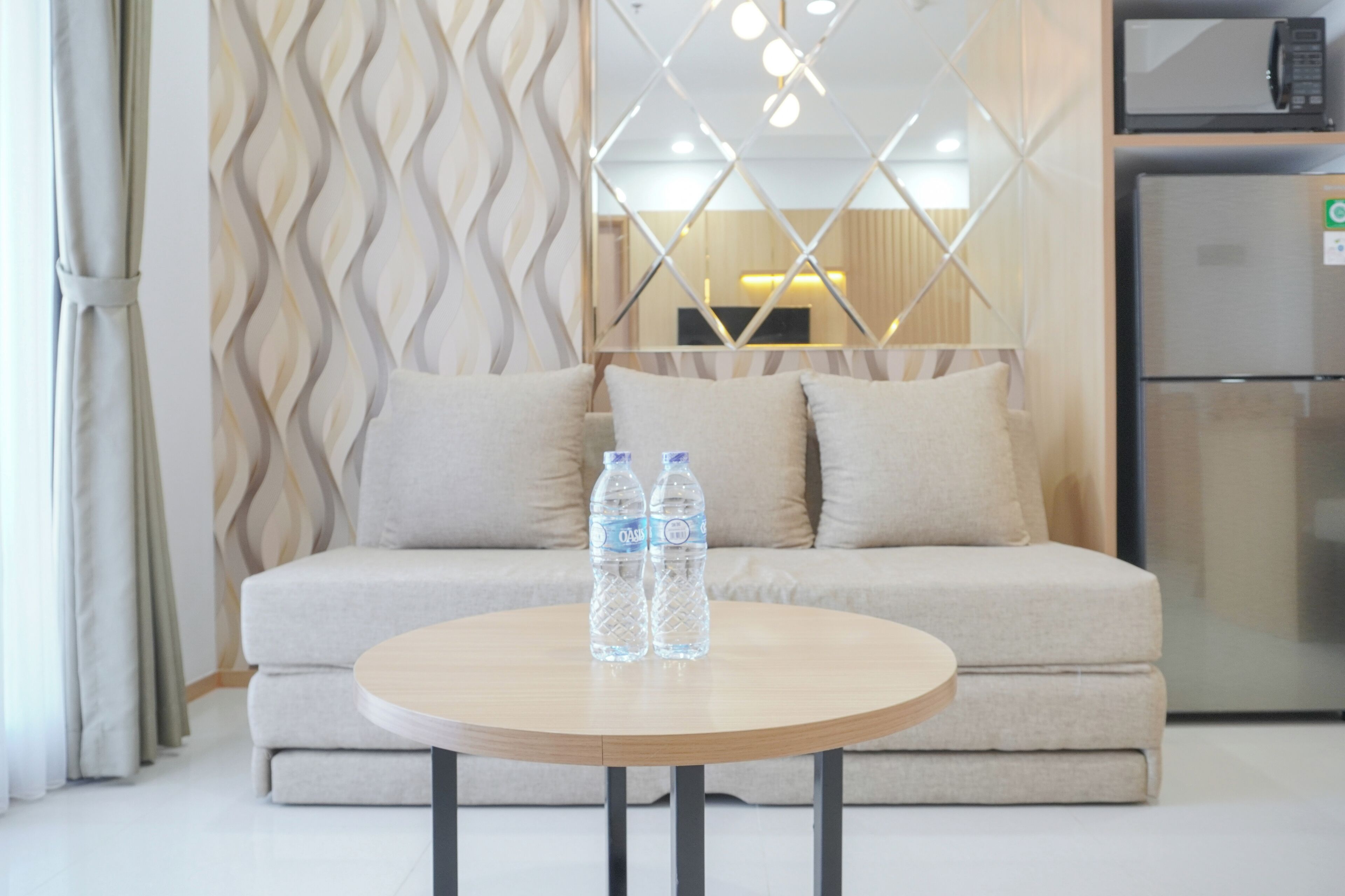 Un salon moderne avec un canapé, deux bouteilles d’eau posées sur une table ronde et un réfrigérateur en arrière-plan.