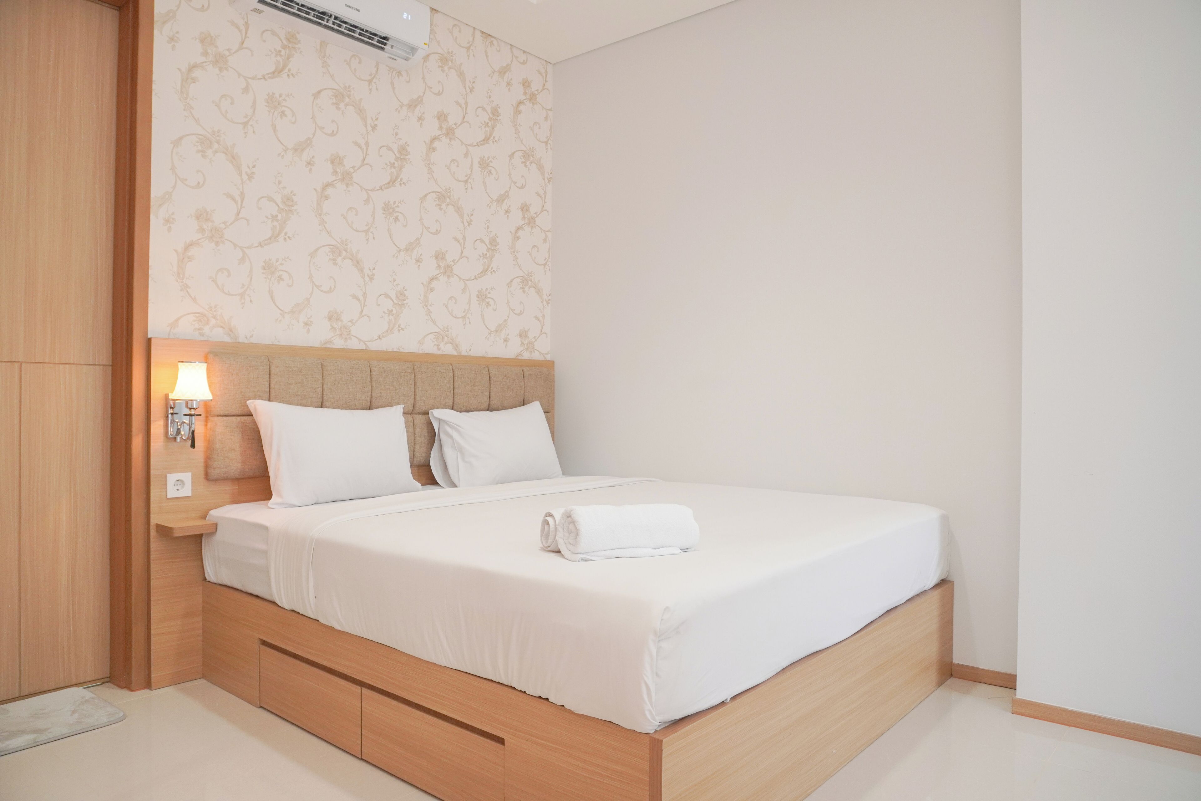 A neatly made bed with a wooden headboard, a bedside table with a lamp, and a patterned wallpaper.