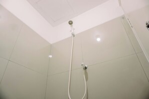 Eine Dusche mit Duschbrause und Wandarmatur, mit gefliesten Wänden und Deckenleuchte.