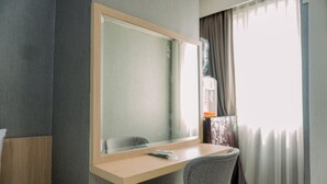 Habitación de hotel con un escritorio de madera, una silla, un espejo grande y un ventanal con cortinas.