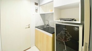 A compact kitchen with a refrigerator, a sink, and a microwave. - Homey 1Br Without Living Room At Amartha View Apartment (Semarang)