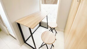 A small, well-lit room with a wooden desk and two stools. - Homey 1Br Without Living Room At Amartha View Apartment (Semarang)