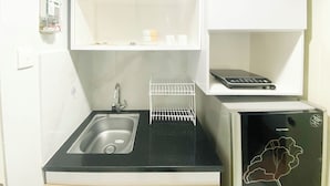 A compact kitchenette with a stainless steel sink, a dish drying rack, and a compact refrigerator. - Homey 1Br Without Living Room At Amartha View Apartment (Semarang)