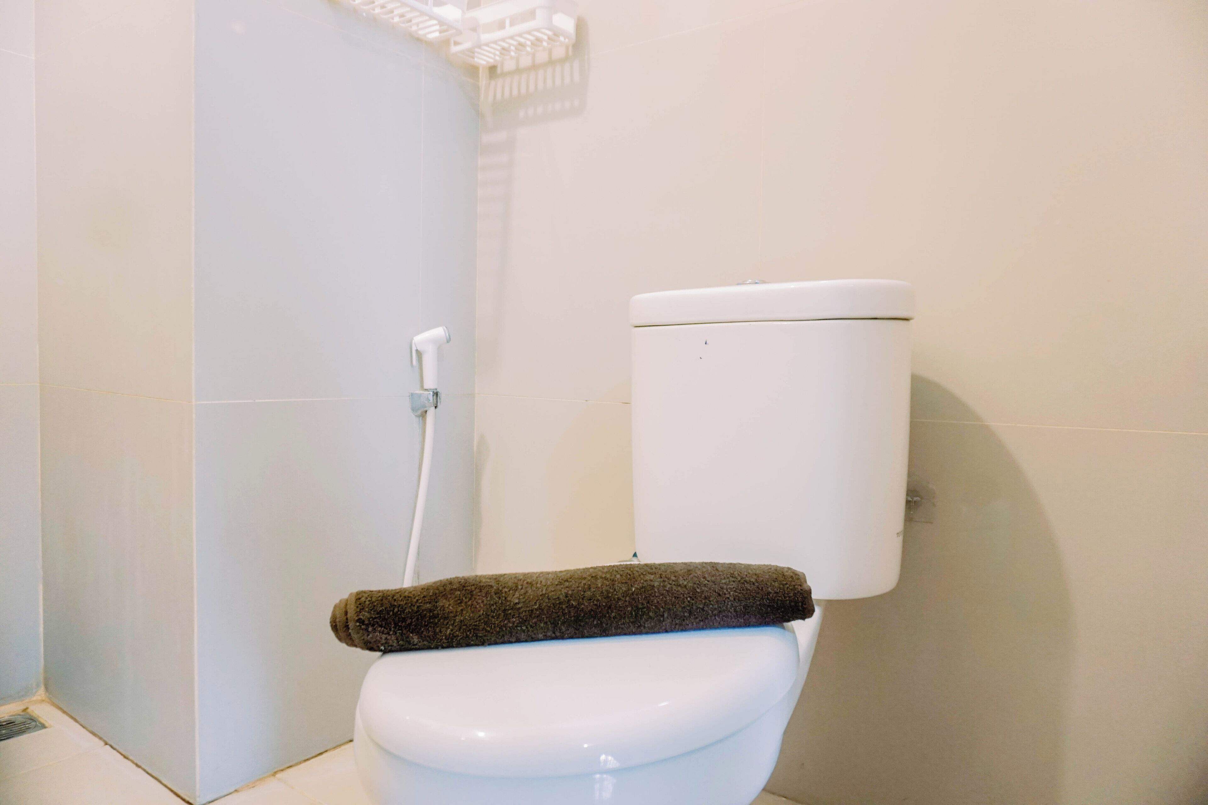 A white toilet with a brown towel on the seat and a white toilet paper holder on the wall.