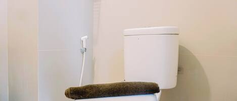 A white toilet with a brown towel on the seat and a white toilet paper holder on the wall.