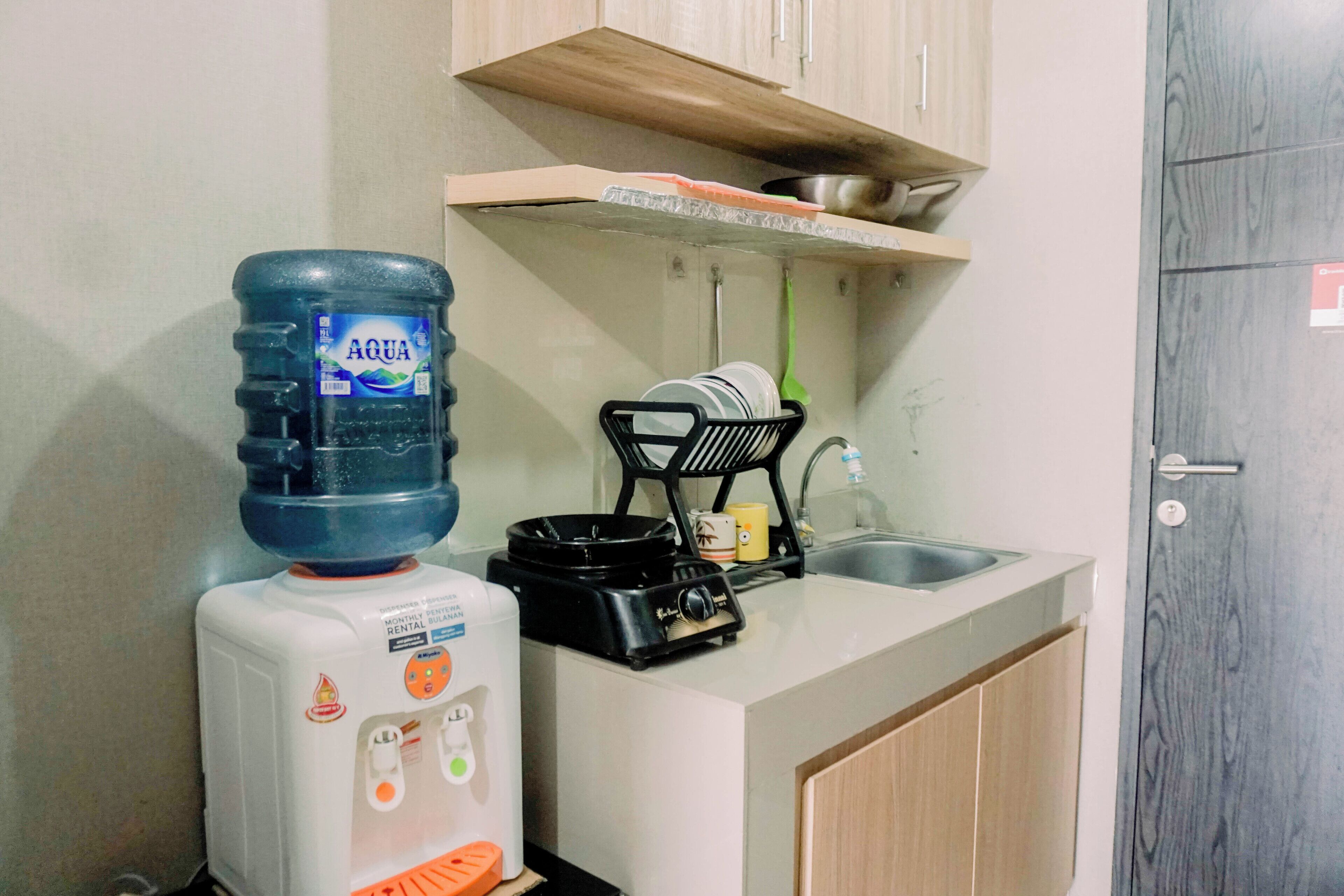 A kitchen with a water dispenser, a rice cooker, a dish rack, and a sink.