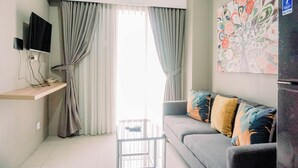 A modern living room with a grey sofa, a mounted TV, and a colorful abstract painting on the wall. - Comfort 2Br At 3Rd Floor Baileys Apartment (South Tangerang)