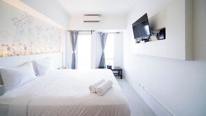 A hotel room with a large bed, a flat-screen TV mounted on the wall, and a window with curtains. - Nice And Comfy Studio At Orchard Supermall Mansion Apartment (Surabaya)