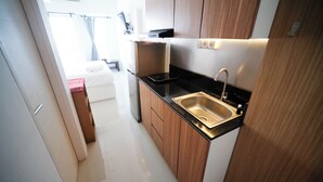 A compact kitchen with a stainless steel sink, wooden cabinets, and a black countertop. - Nice And Comfy Studio At Orchard Supermall Mansion Apartment (Surabaya)