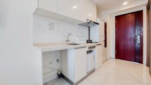 A modern kitchen with white cabinets, a marble countertop, a built-in oven, and a red door. - Cozy And Comfort Studio Sky House Alam Sutera Apartment (Tangerang)