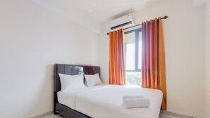 A neatly made bed with white linens and a folded towel, a dark headboard, and orange curtains on a window. - Cozy And Comfort Studio Sky House Alam Sutera Apartment (Tangerang)