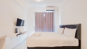A hotel room with a bed, a TV on a shelf, and an air conditioning unit. - Homey And Simply Look Studio Sky House Alam Sutera Apartment (Tangerang)