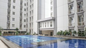 Une piscine entourée d’un bâtiment moderne doté de nombreux balcons et de plusieurs unités de climatisation.