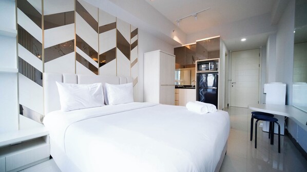 A modern hotel room with a large bed, a desk, and a kitchenette.