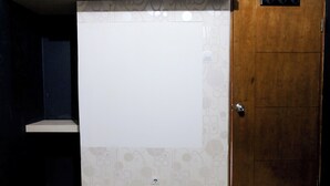 A room with a white tiled wall, a wooden door, and a small shelf. - Tranquil Designed 2Br At Gateway Ahmad Yani Cicadas Apartment (Bandung)
