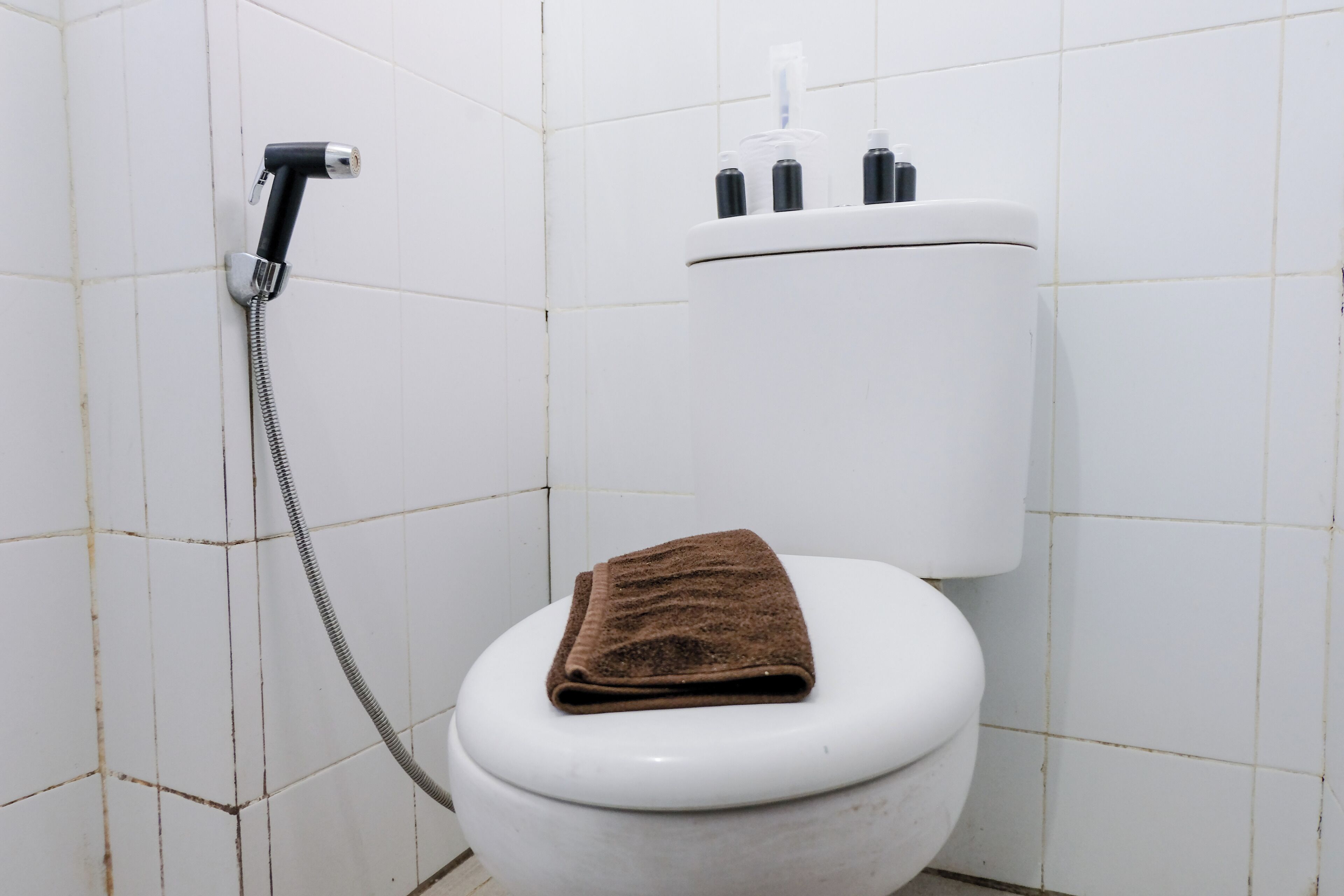 A white toilet with a brown towel on the seat and a showerhead mounted on the wall.