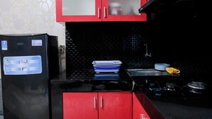 A kitchen with red cabinets, a black refrigerator, and a black tiled backsplash. - Tranquil Designed 2Br At Gateway Ahmad Yani Cicadas Apartment (Bandung)