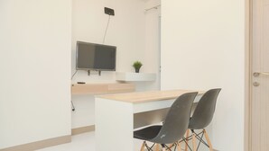A modern, minimalist room with a white desk, two black chairs, a mounted TV, and a small potted plant. - Fancy And Nice 2Br Apartment At Tokyo Riverside Pik 2 (Teluknaga)