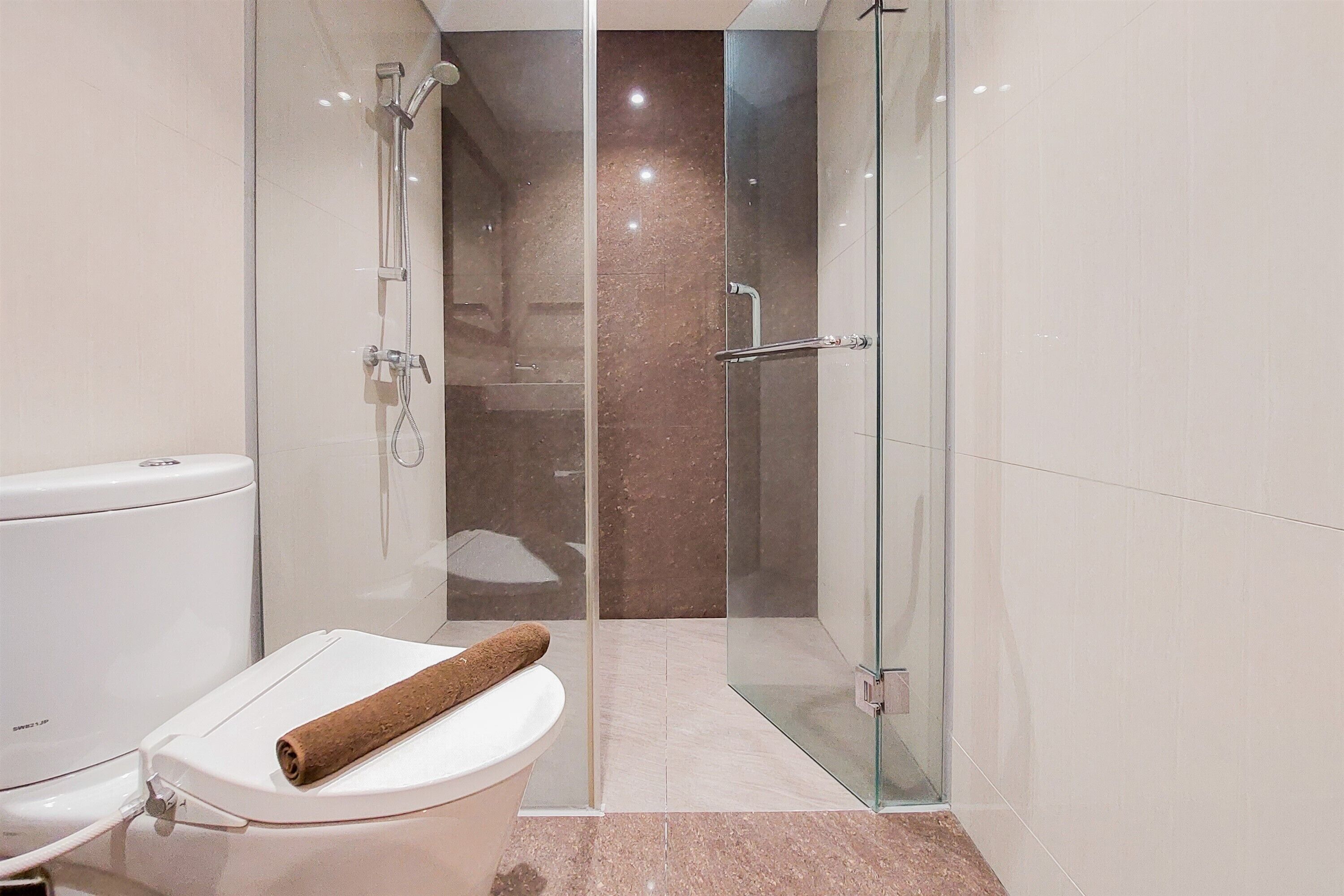 Une salle de bain moderne avec une douche à parois de verre, des toilettes avec un porte-serviette et un sol en marbre.