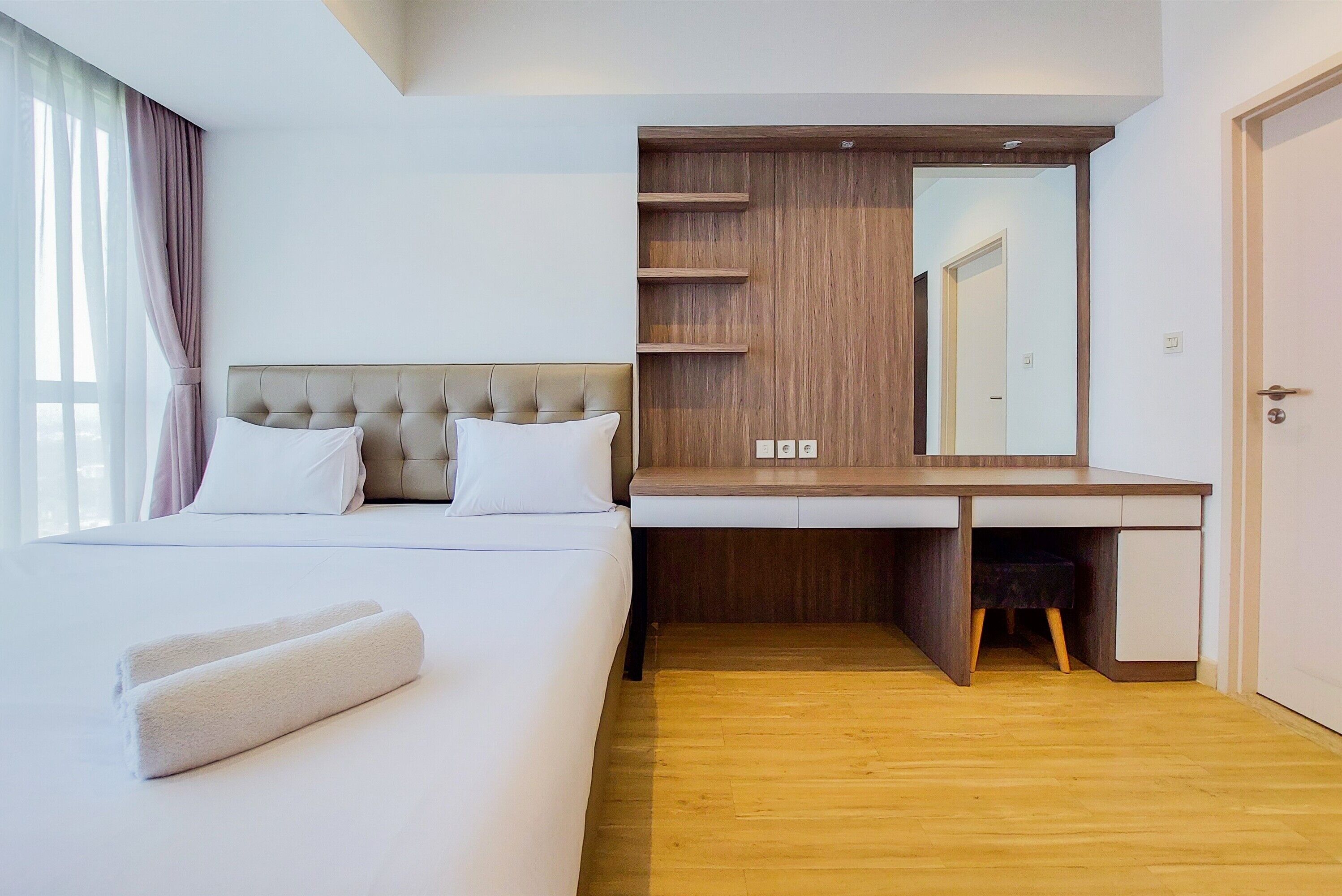 A hotel room with a bed, a wooden desk, and a large mirror.