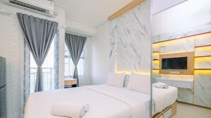 A modern hotel room with a large bed, a flat-screen TV mounted on a marble wall, and a small bedside table. - Cozy Stay And New Furnished Studio At Transpark Cibubur Apartment (Depok)