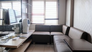 A modern living room with a sofa, a desk with a computer, and a standing fan. - Spacious 3Br Combined Unit At Pinewood Apartment (Cileunyi)