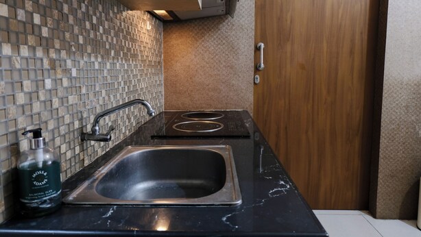 A modern kitchen with a black countertop, stainless steel sink, and a tiled backsplash. - Spacious 3Br Combined Unit At Pinewood Apartment (Cileunyi)