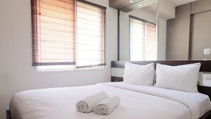 A neatly made bed with white linens and two rolled towels, a large mirror on the wall, and a window with blinds. - Spacious 3Br Combined Unit At Pinewood Apartment (Cileunyi)