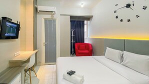 Een hotelkamer met een bed, een bureau, een televisie, een rode stoel en een klok aan de muur.