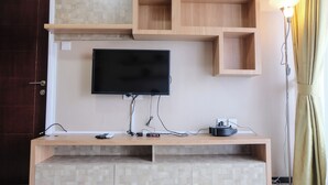 A modern living room with a mounted TV, wooden shelving, and a floor lamp. - Cozy 2Br Apartment At Gateway Pasteur (Cimahi)