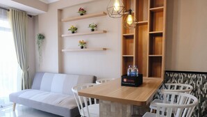 A modern living room with a sofa, dining table, chairs, and a built-in bookshelf. - Cozy 2Br Apartment At Gateway Pasteur (Cimahi)