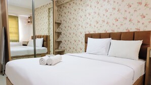 A neatly made bed with white linens and pillows, a wooden headboard, and a floral wallpaper pattern. - Cozy 2Br Apartment At Gateway Pasteur (Cimahi)