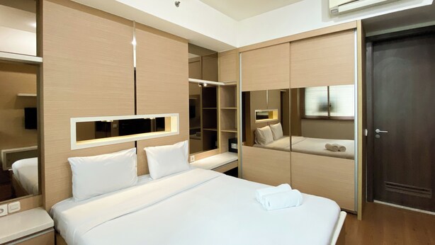 A modern hotel room with a large bed, built-in wardrobe, and a mirror. - Modern Look And Comfort 2Br Kemang Village Apartment (Jakarta)